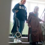Aidante accompagnant une femme âgée pour descendre les escaliers de son immeuble