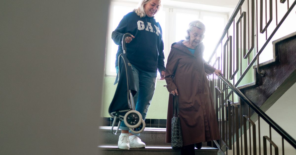 Aidante accompagnant une femme âgée pour descendre les escaliers de son immeuble