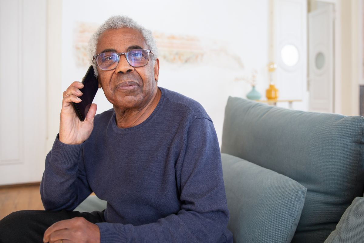 Elderly man talking on the phone sitting on his home sofa