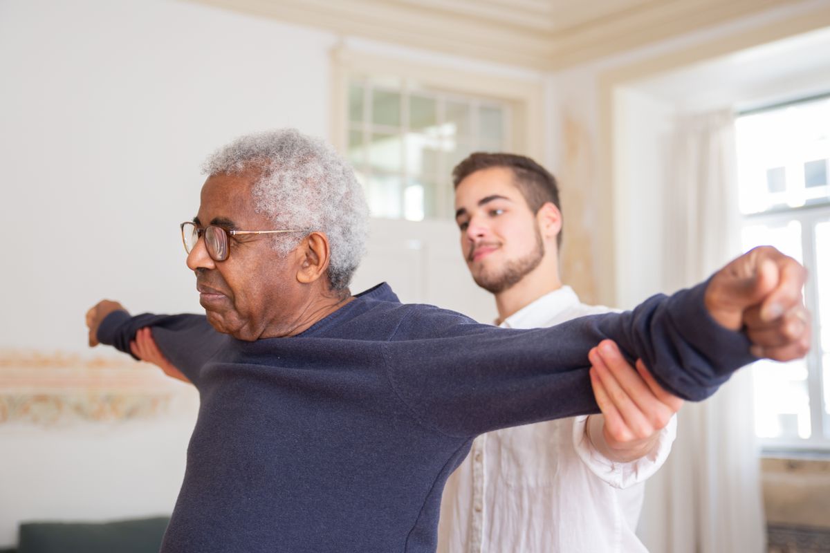Elderly man doing arm exercises at home with the help of another person
