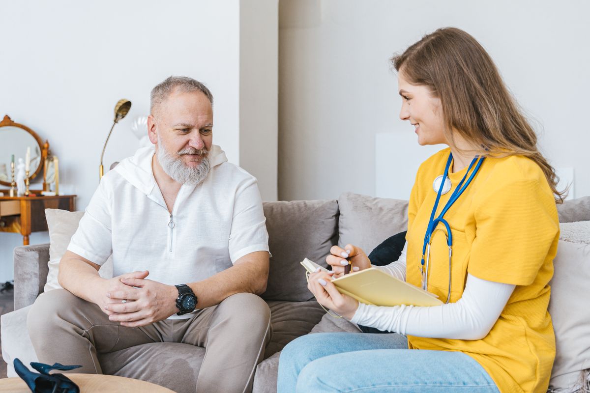 Healthcare professional taking notes during a home visit to an elderly man
